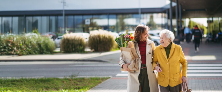 mature granddaughter carrying groceries out to her grandmother's car. senior woman shopping at the shopping center, needing help loading groceries into car.